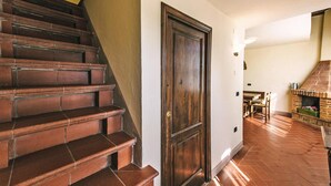 Eine Treppe mit Holzbodenstufen führt zu einer Tür, einem Kamin aus Ziegeln und einem Essbereich mit Tisch und Stühlen.