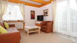 A living room with a sofa, armchair, TV, and artwork on the wall. - Appartementhaus auf Pellworm (Pellworm)