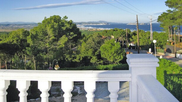 Uma varanda com vista para uma paisagem costeira, incluindo árvores, uma linha de costa distante e uma estrutura de linha de energia.