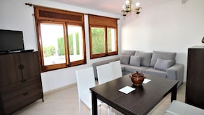 Uma sala de estar com sofá, mesa de jantar e televisão sobre um móvel.
