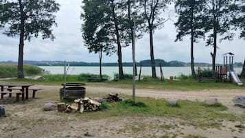 A lakeside campsite with picnic tables, a fire pit, and a playground.