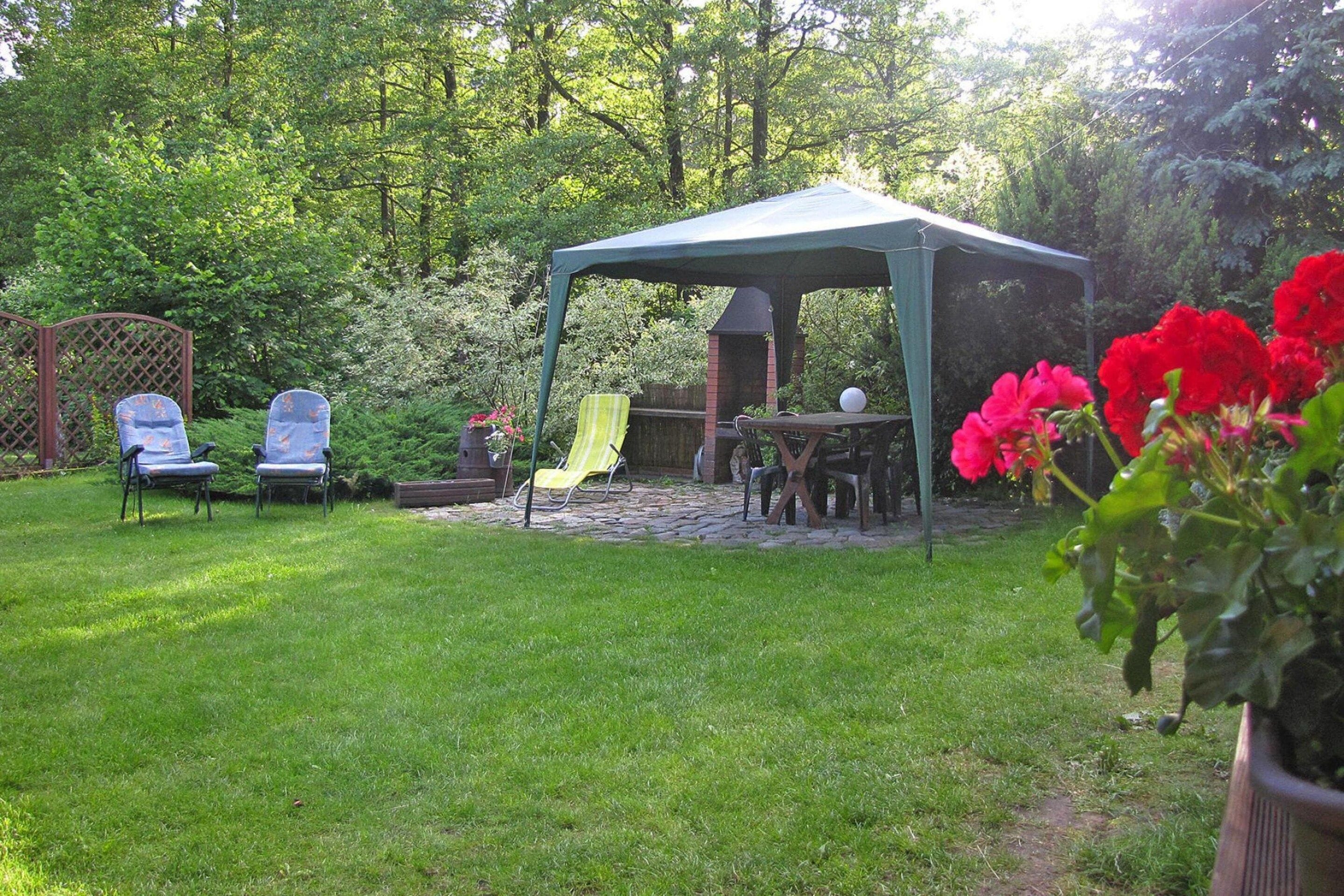 Een overdekt terras met een tafel en stoelen, omgeven door een weelderige tuin en een barbecue van baksteen.