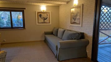 A room with a grey sofa, a wooden ceiling, a white brick wall, and two framed pictures.