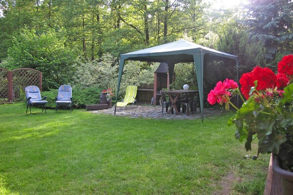 A covered patio area with a table and chairs, surrounded by lush greenery and a brick fire pit. - Wooden House by Masurian Lakes Gizycko (Gizycko)