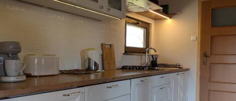 A kitchen with white cabinets, a wooden countertop, a coffee maker, a toaster, and a window above the sink.