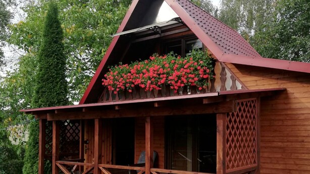 A wooden cabin with a balcony adorned with red flowers, a wooden porch, and a lattice door. - Wooden House by Masurian Lakes Gizycko (Gizycko)