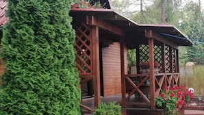 A wooden deck with a lattice railing, surrounded by lush greenery and flowering plants. - Wooden House by Masurian Lakes Gizycko (Gizycko)