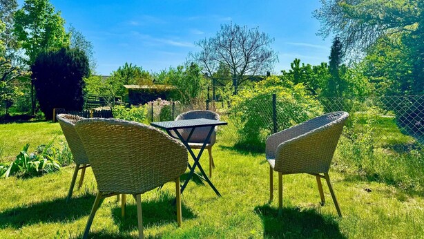 A garden with wicker furniture and a table, surrounded by greenery and trees. - Ferienhaus Havelzeit in Werder an der Havel (Werder (Havel))