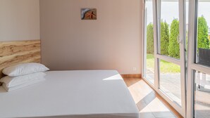A modern bedroom with a large bed, a wooden headboard, a small painting, and a sliding glass door leading to a balcony with greenery. - Holiday Homes With Pool, Close to the Beach (Ustronie Morskie)