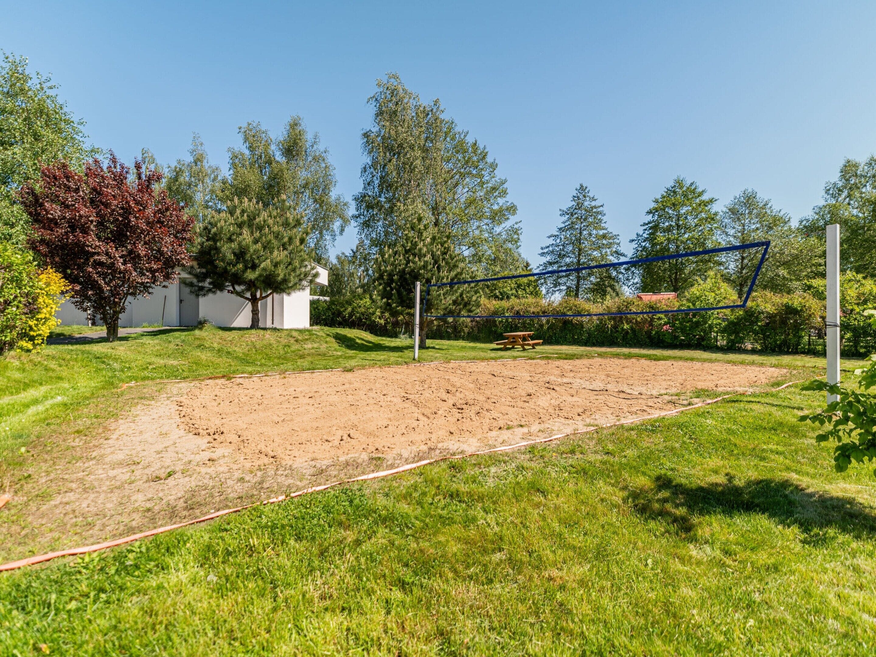 Una cancha de voleibol con una mesa de picnic y un edificio pequeño al fondo.