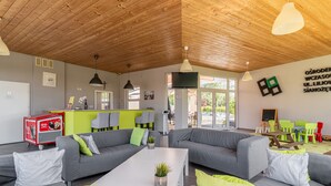 A modern living room with grey sofas, a white coffee table, and bright green cushions. There is a kitchen area with a red cart and a bar counter. The room has wooden ceilings and large windows. - Holiday Homes With Pool, Close to the Beach (Ustronie Morskie)