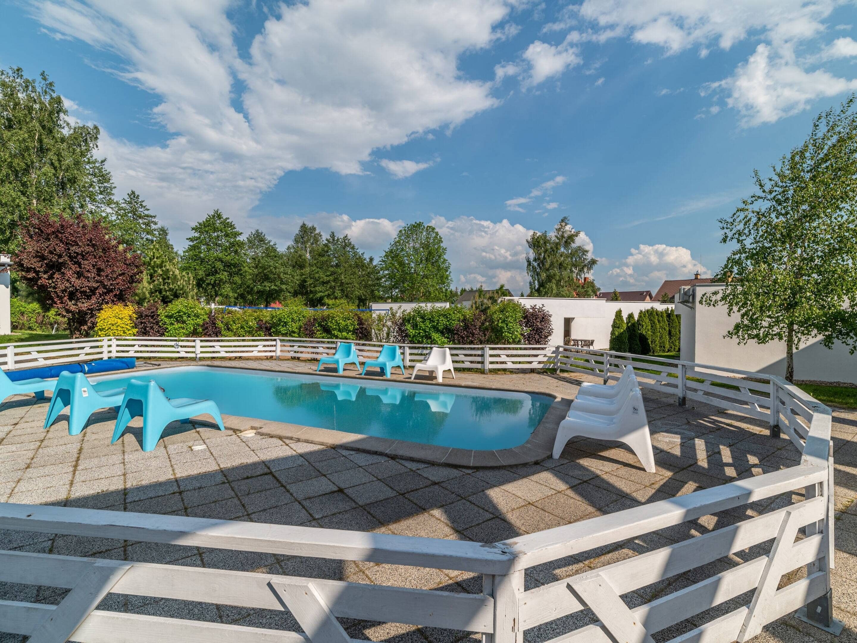 A swimming pool with a white fence, blue chairs, and a clear sky.