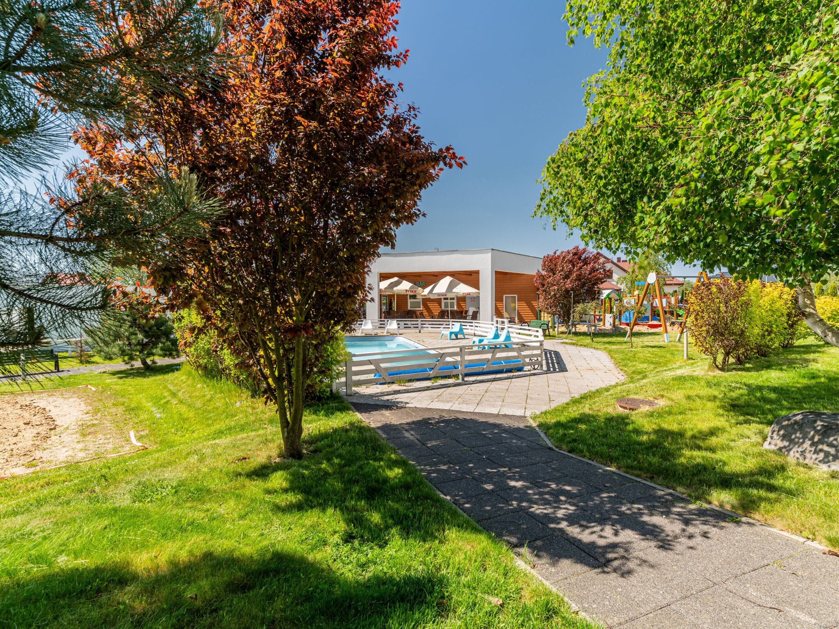 A pathway leading to a building with outdoor seating and a pool area.