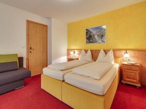 A double bed with two bedside tables, a wooden door, a sofa, and a yellow wall with a picture. - Apartment in Fugen Near Spieljochbahn (Fuegen)