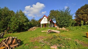 A house with a red roof, surrounded by a grassy area with trees and a pile of firewood. - Comfortable Holiday Home With a Garden, Noskowo (Slawno)