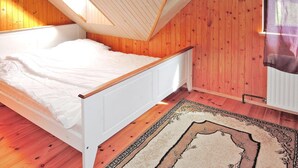 Une chambre avec un plafond en pente, des murs en bois, un lit blanc et un tapis à motifs.
