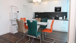 Une cuisine moderne avec des meubles blancs, un micro-ondes noir et un coin repas comprenant une table blanche et des chaises colorées.