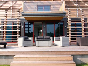 A modern house with a wooden exterior, a balcony with wicker furniture, and large glass doors. - Chalet mit Aussensauna in Wendorf (Kuhlen-Wendorf)