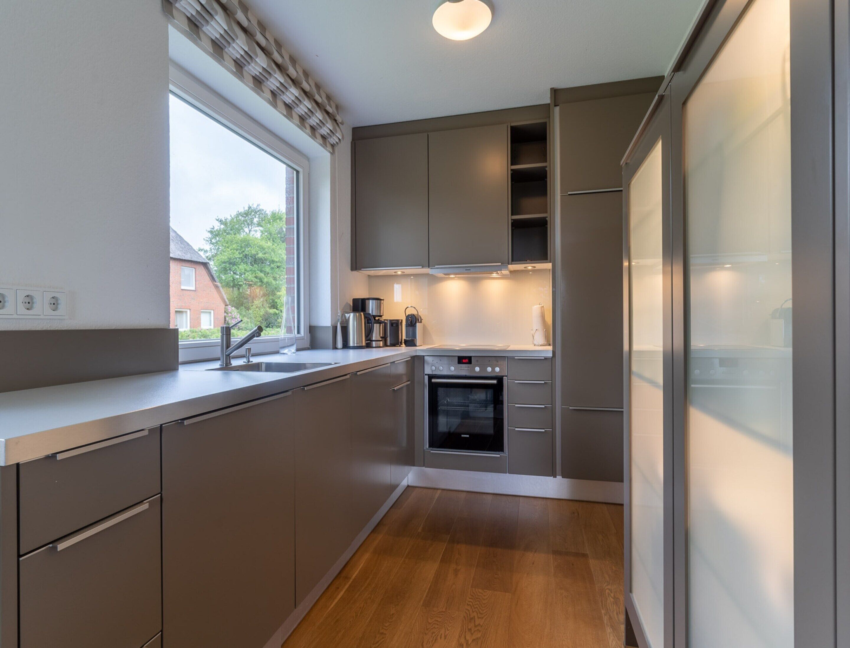 A modern kitchen with a built-in oven, stainless steel appliances, and a window with a view of the outside.