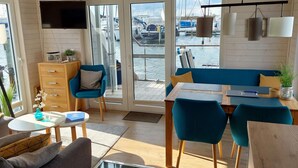 A modern interior with a wooden floor, a dining area with blue chairs, a sofa, and a TV mounted on the wall. - Houseboat Hecht in Egernsund at the Marina Minde (Broager)