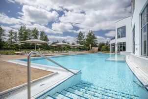 Una piscina con un borde de baldosas, sillas de descanso y sombrillas.