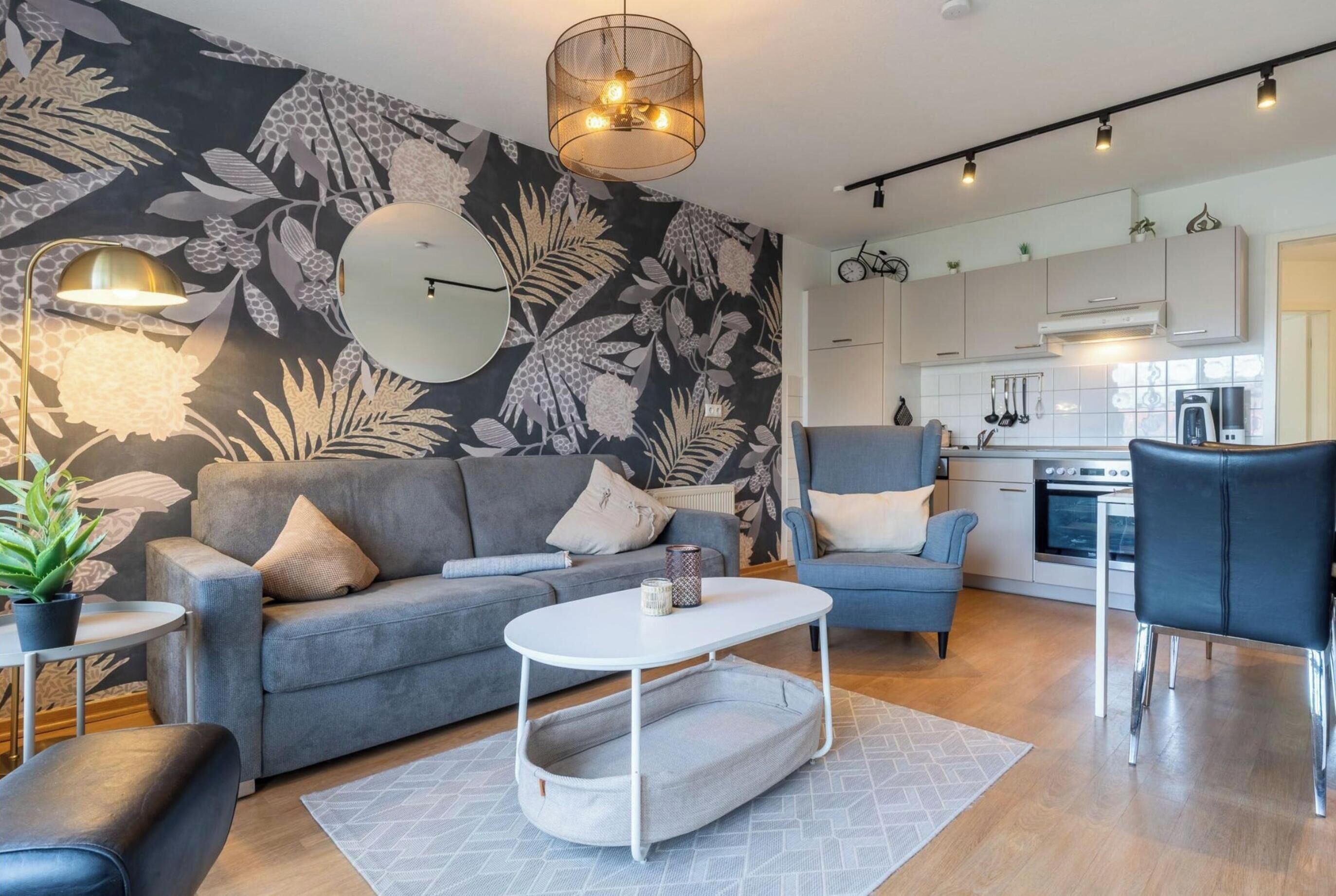 A modern living room with a grey sofa, a white coffee table, and a kitchen in the background.