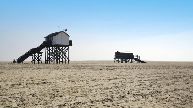 Una playa con dos estructuras de madera, una con escalones y otra con techo plano.