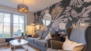 Una sala de estar moderna con un sofá gris, una mesa redonda y un gran papel tapiz con estampado floral.