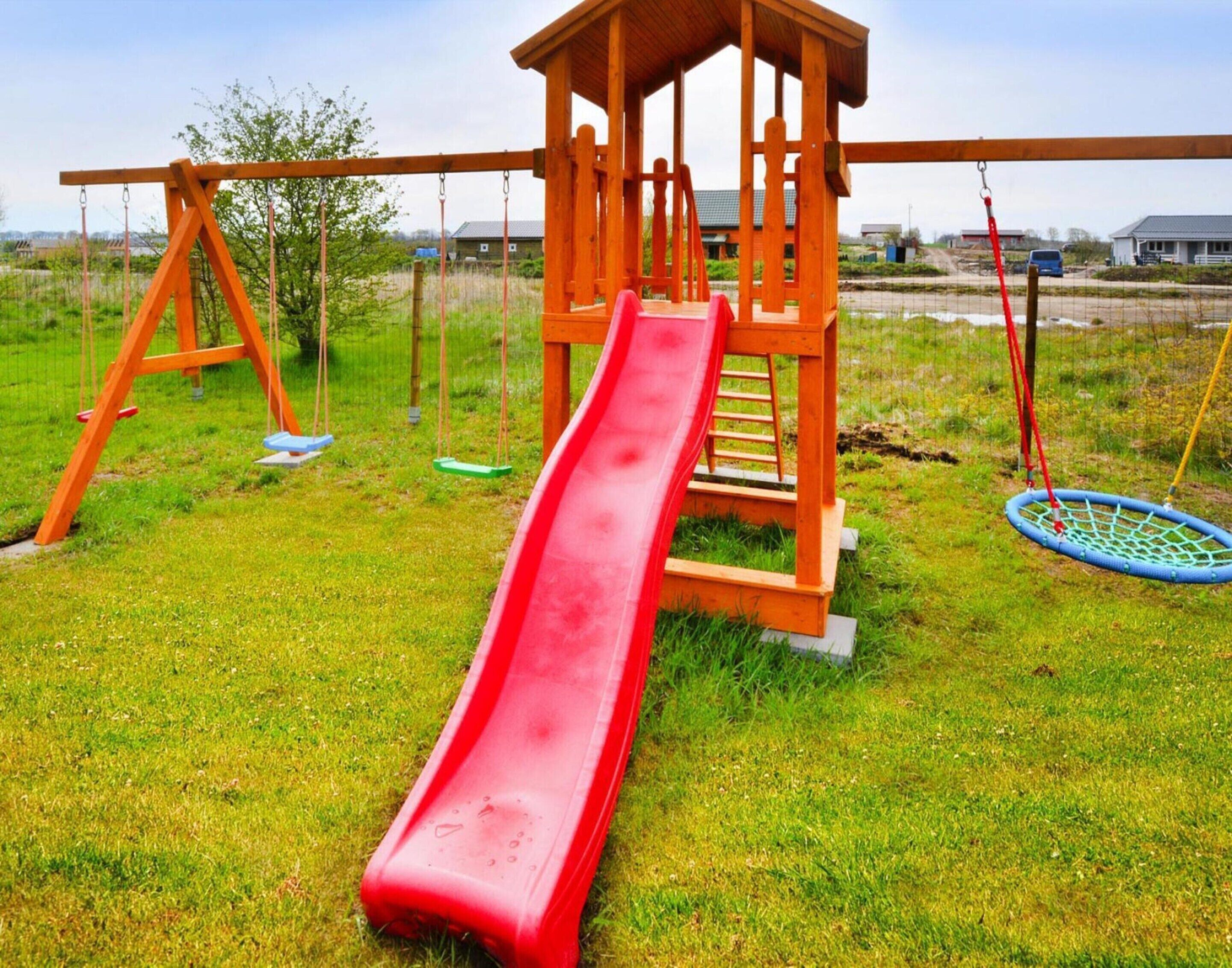 Une aire de jeux avec un toboggan rouge, des balançoires et une structure d’escalade.