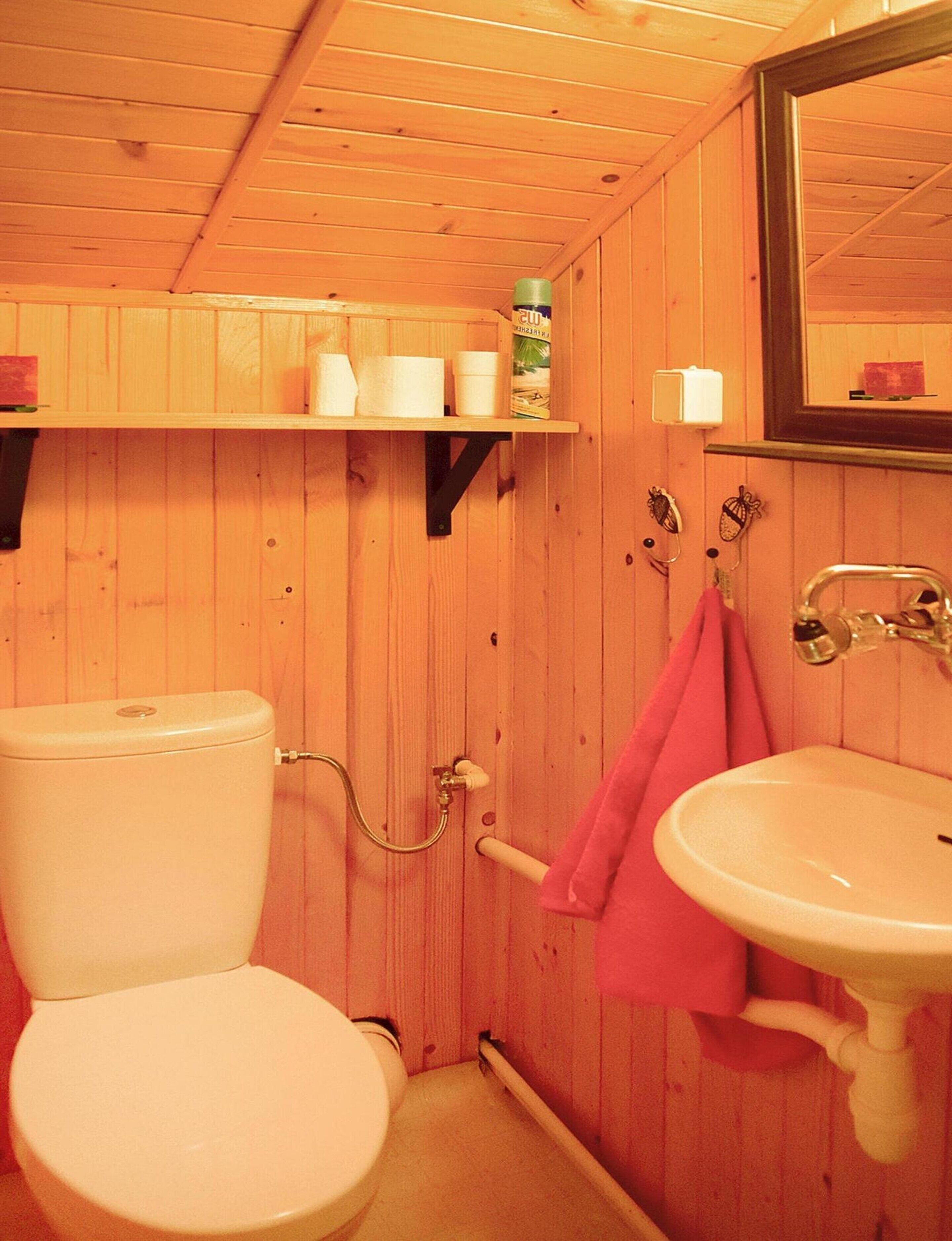 A wooden-paneled bathroom with a toilet, sink, and shelves holding toiletries.