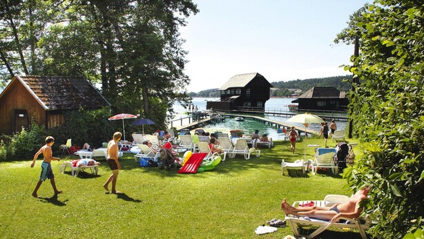 A lakeside outdoor area with lounge chairs, umbrellas, and a dock extending into the water. - Sunny Holiday Apartment With Balcony on Klopeinersee With Private Beach (Sankt Kanzian am Klopeiner See)