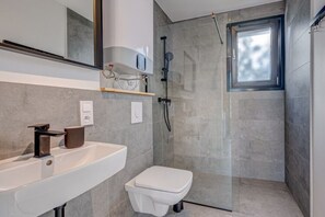 A modern bathroom with a white sink, a toilet, and a glass-enclosed shower area. - Cottage in Pustkowo Near Sandy Beach (Rewal)