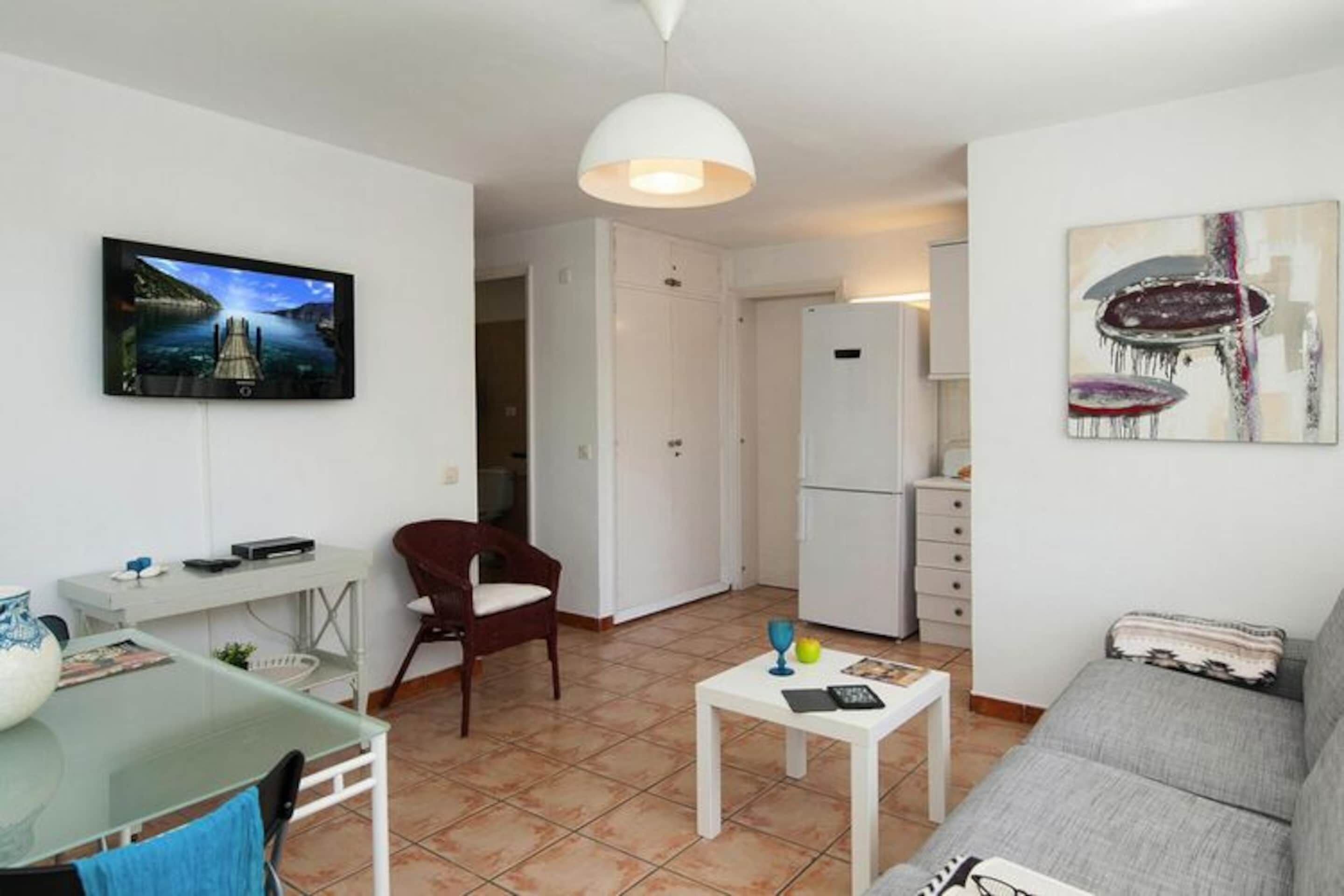 Ein modernes Wohnzimmer mit Flachbildfernseher, einem Glastisch, einer Couch und einem kleinen Couchtisch.