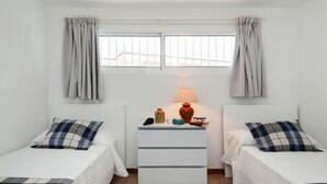 A small, clean room with two beds, a nightstand, a lamp, and a window with curtains.