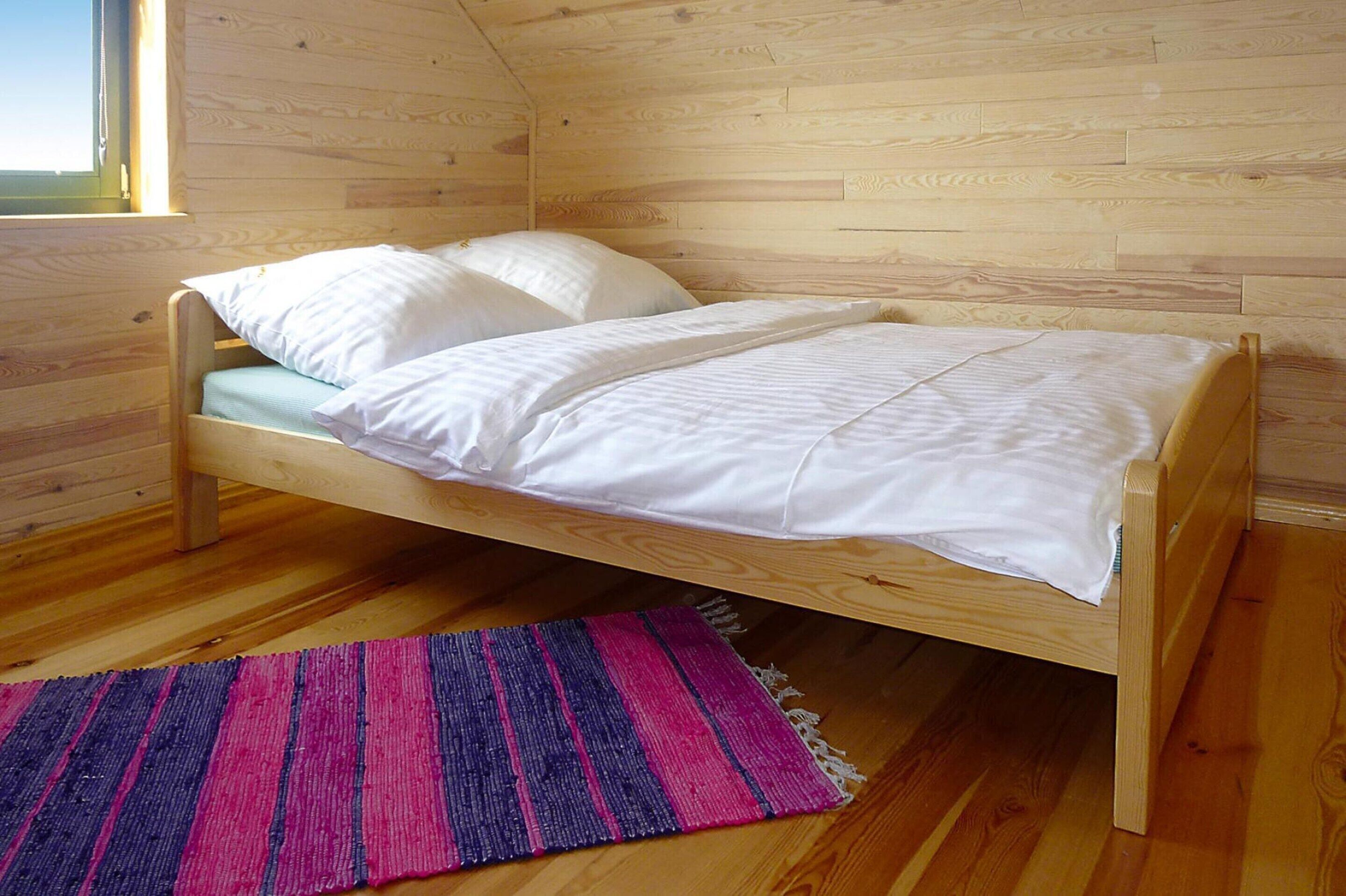 A single wooden bed with white bedding in a room with wooden walls and floors.