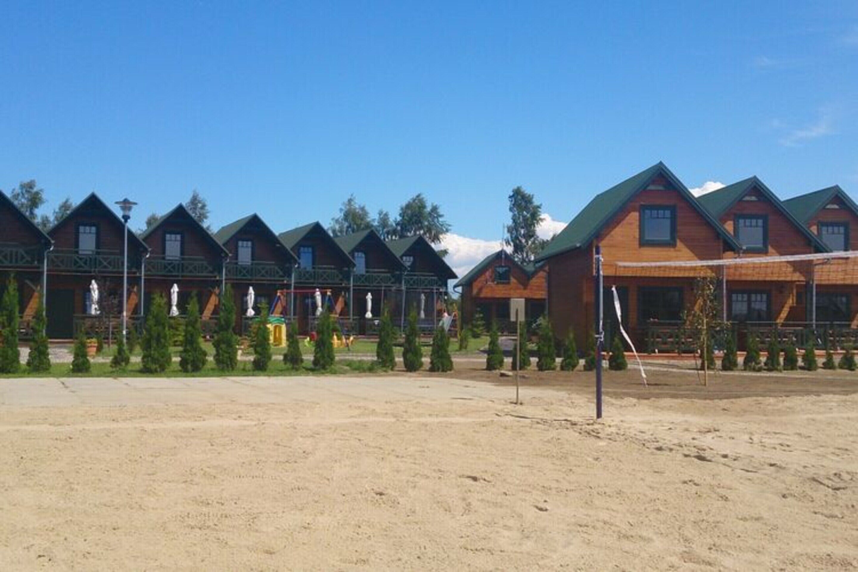 Una hilera de cabañas de madera con techos verdes, dispuestas en fila, con una red de voleibol al frente.