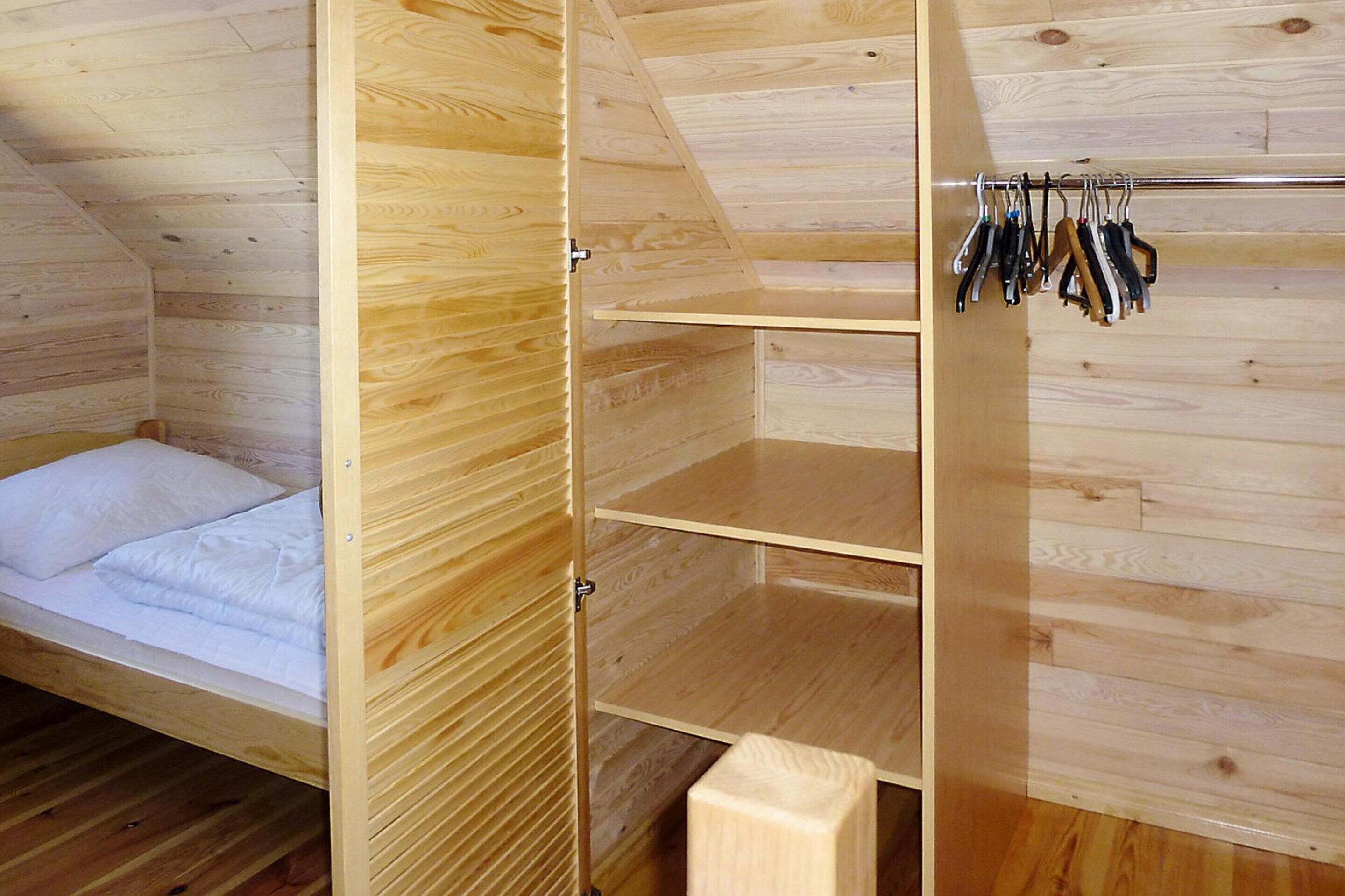 Une pièce en bois avec un lit, une armoire où sont suspendus des vêtements et une étagère.