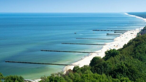 A coastal beach with a long pier extending into the water, surrounded by lush greenery. - Beautiful Apartment Very Close to the Beach (Rewal)