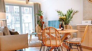 A modern living room with a sofa, dining table, and chairs. There are potted plants and a vase with flowers on the table. - Beautiful Apartment Very Close to the Beach (Rewal)