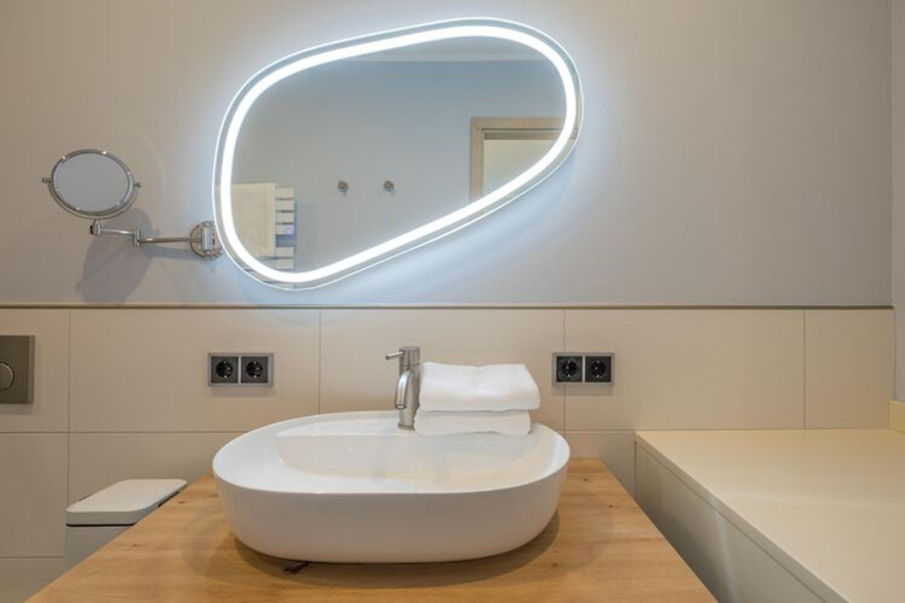 Un bagno moderno con uno specchio rotondo, un lavabo bianco e un mobile contenitore in legno.