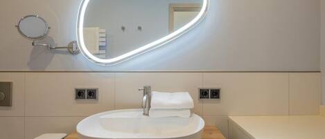 Un bagno moderno con uno specchio rotondo, un lavabo bianco e un mobile contenitore in legno.