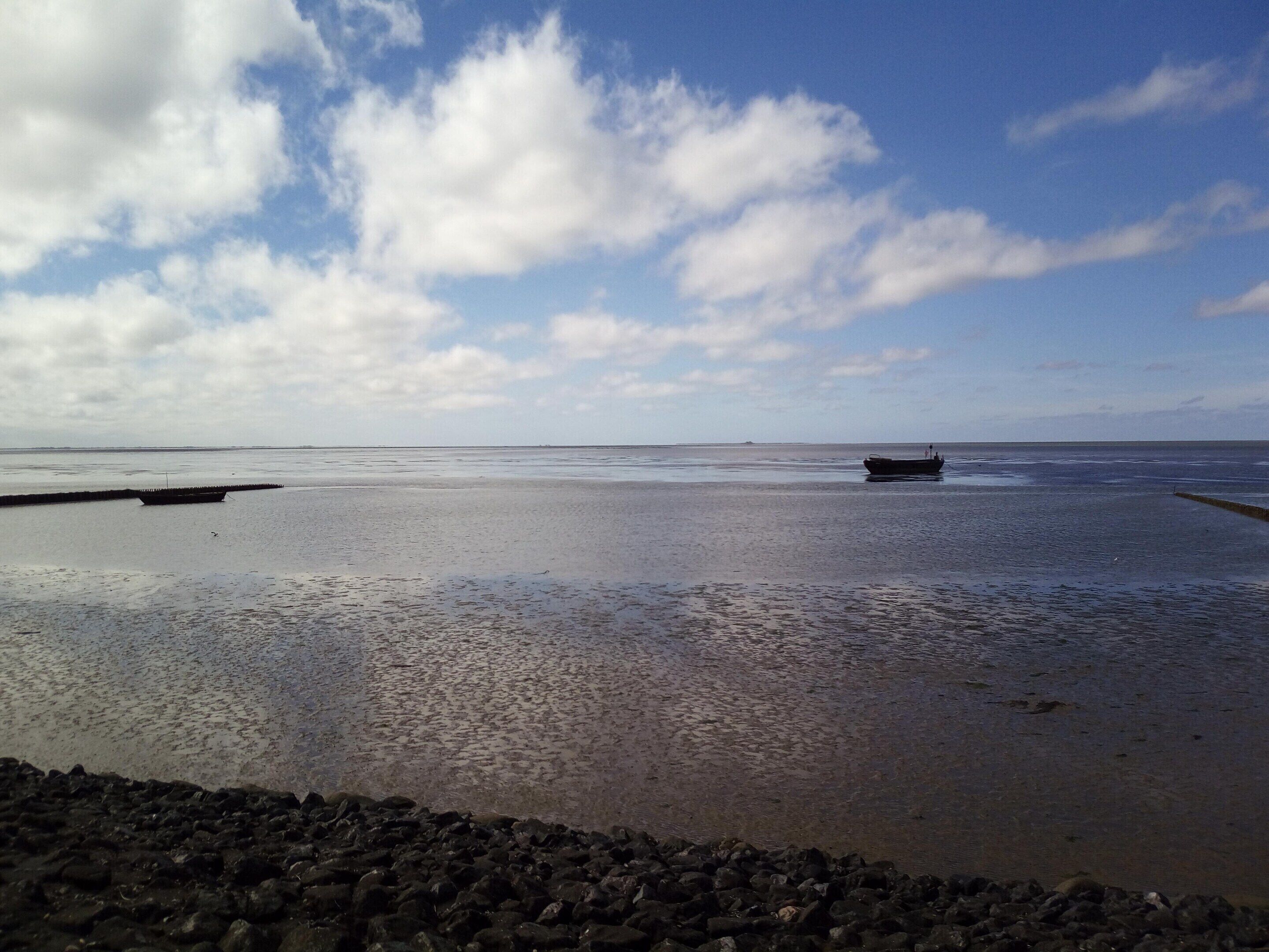 A beach with calm waters, a boat, and a rocky shoreline.
