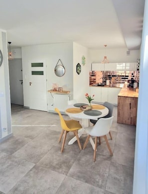 A modern kitchen with white cabinets, a wooden countertop, and a dining area with a round table and chairs. - Comfortable Apartment With a Terrace in Mielno (Mielno)