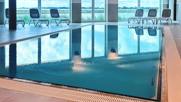 Una piscina interior con vistas despejadas al exterior, rodeada de sillones de descanso.