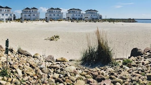 Un hotel frente a la playa con varias edificaciones blancas, una playa de arena y un primer plano rocoso.