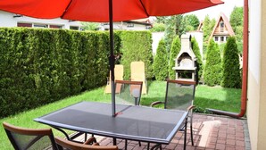 Une terrasse avec une table et des chaises, un parasol rouge et un barbecue.
