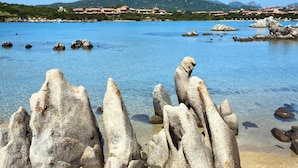 Eine Küstenlandschaft mit klarem, blauem Wasser, Felsformationen und einem fernen Gebirgszug.