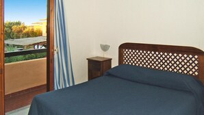 Ein Schlafzimmer mit Bett, Nachttisch, Fenster mit Blick auf Grünflächen und einem Balkon.