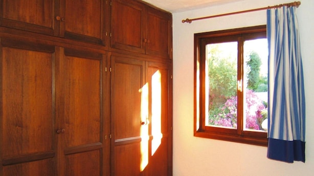 Ein Schlafzimmer mit Bett, Holzschrank und einem fenster mit Vorhängen.
