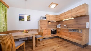 Eine moderne Küche mit Holzschränken, einem Esstisch mit Stühlen, einer Obstschale und einer Mikrowelle.